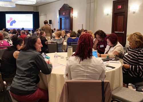Healthcare educators collaborating in small groups at round tables during a workshop session