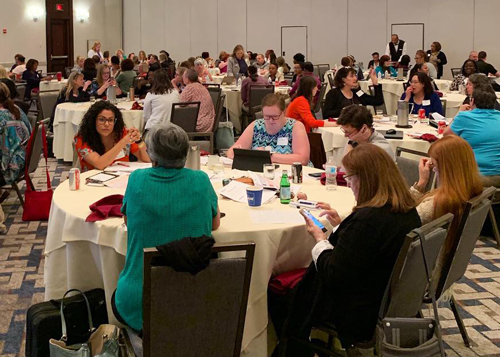 Large conference room of healthcare educators seated at round tables participating in a training session